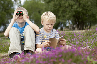 Two children sitting in heathland, one with binoculars and one with a Wildlife Watch book