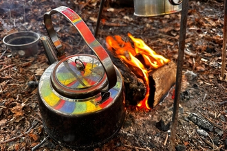 Campfire and teapot which has a rainbow reflection on it. They are laid on the woodland floor for forest school