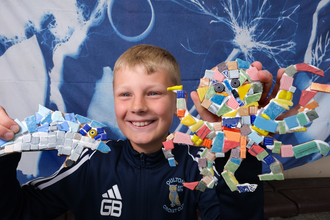 boy smiling and holding up 2 mosaics he's made of a dolphin and an octopus.