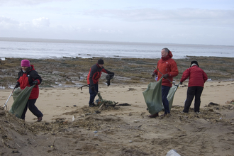 a group of 4 people with litter pickers and bin bags clean the beach