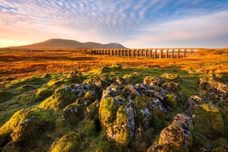 view of a viaduct railway bridge over the imestone pavement Yorkshire Dales with a mountain in the distance. 