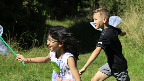 Two children running in the sunshine with butterfly nets