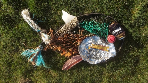Marine litter arranged into the shape of a fish including nets and crisp packets