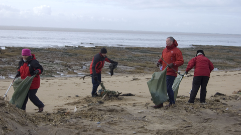 a group of 4 people with litter pickers and bin bags clean the beach