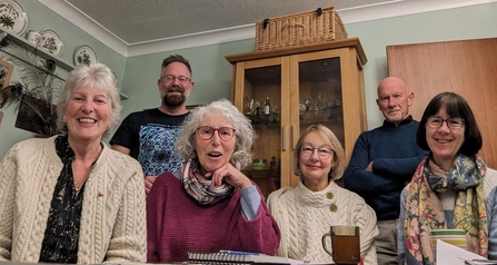 Group photo of a community group taking action for nature. They are sat around a table in a kitchen.