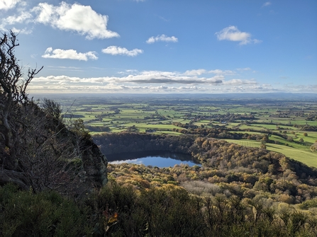 View from a high hilltop nature reserve looking down onto the lake below. It's a sunny day with little cloud in a blue sky.