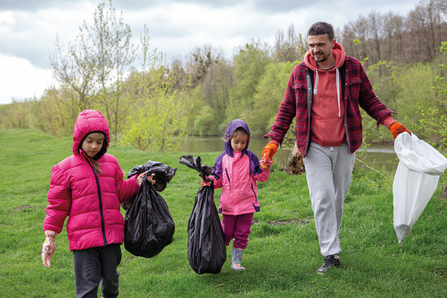 Family litter-picking on grassy gorund carrying bags and wearing coats.