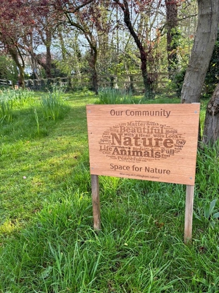 Word cloud generated from residents reasons to love nature depicted on a wooden board stading at the entrance to a woodland on overgrown verges next to a mown oath into the woodland.