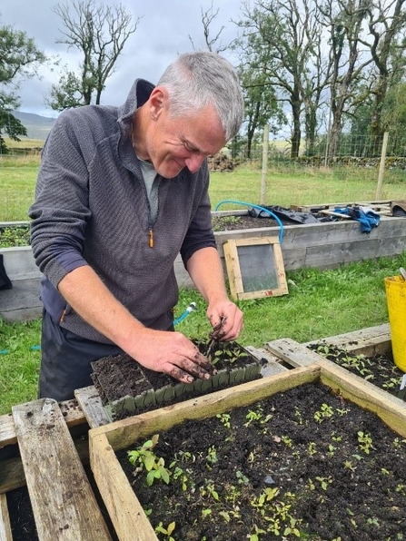 Man stood potting out seedlings at a table in a field