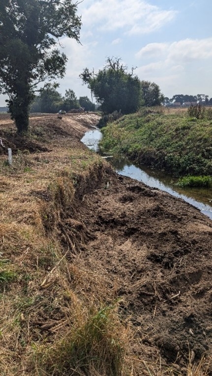 The river foss winds past a brown and heavily eroded bank (left)