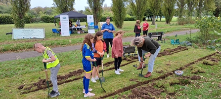 group of children and a couple of adults digging long beds to plant bulbs in on a community park