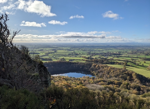 View from a high hilltop nature reserve looking down onto the lake below. It's a sunny day with little cloud in a blue sky.